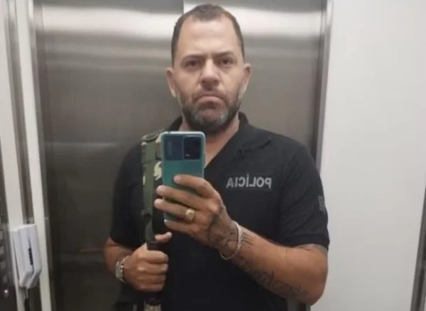 Imagem de homem com uniforme de policial penal com celular na mão - Metrópoles