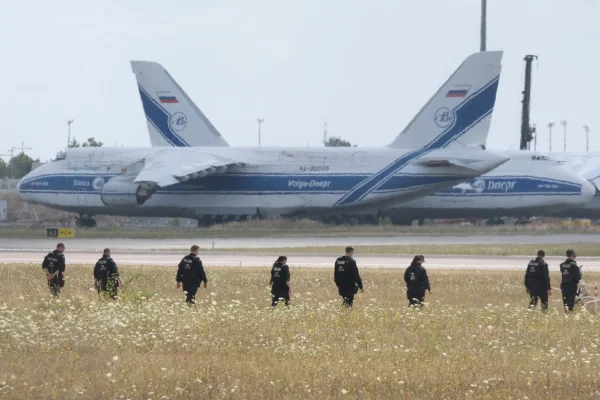 Policiais caminham por um campo nas dependências do Aeroporto de Leipzig. A investigação sobre a descoberta do drone carregado de explosivos está em andamento. Vários policiais estão no local, próximo à pista norte, realizando buscas a pé.