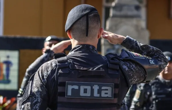 Em foto colorida PM de costas faz continência com a palavra rota escritas nas costas e usando boina - Metrópoles