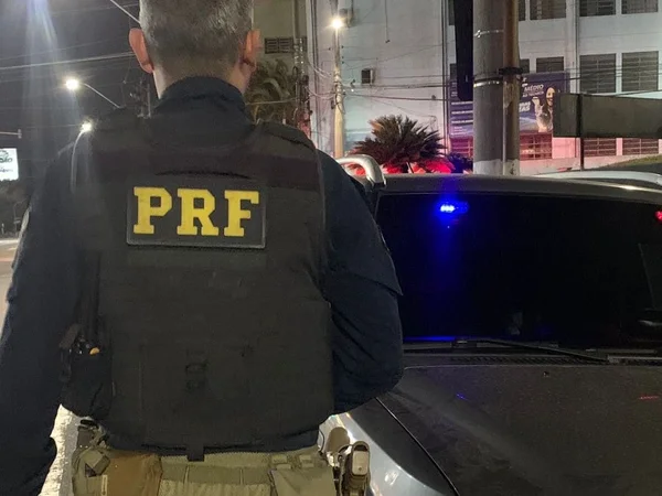 Imagem colorida mostra agente da Polícia Rodoviária Federal de costas, próximo a um carro cinza escuro - Metrópoles