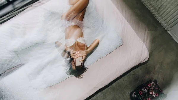 Mulher de lingerie na cama com celular