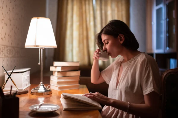 Mulher lendo livro e tomando uma xícara de café a noite - Metrópoles