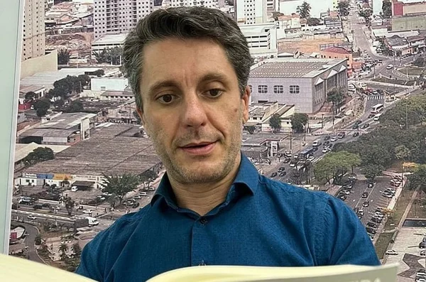 Homem branco com cabelo grisalho e camisa azul olha para baixo, lendo um livro - Metrópoles