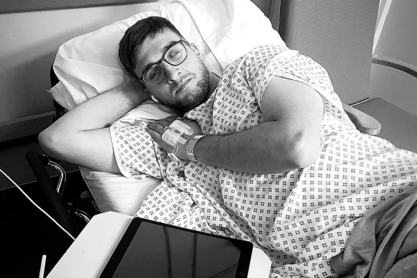 Foto em preto e branco de homem deitado em maca, de um ambiente hospitalar - Metrópoles.
