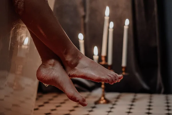 Pés molhados pendurados na banheira com velas acesas ao fundo - Metrópoles