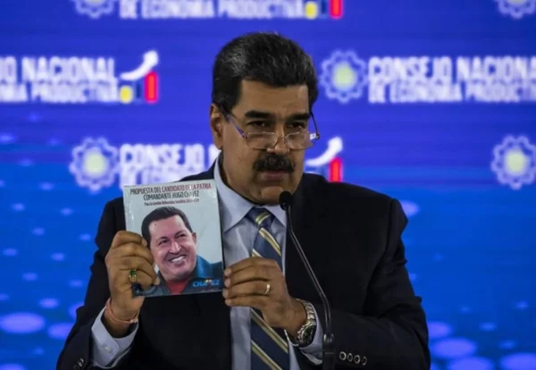 Foto colorida de Nicolás Maduro segurando um livro com foto do Hugo Chávez - Metrópoles