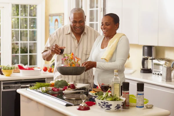 Casal negro está sorrindo e preparando uma comida saudável, cheia de verduras, legumes - Metrópoles