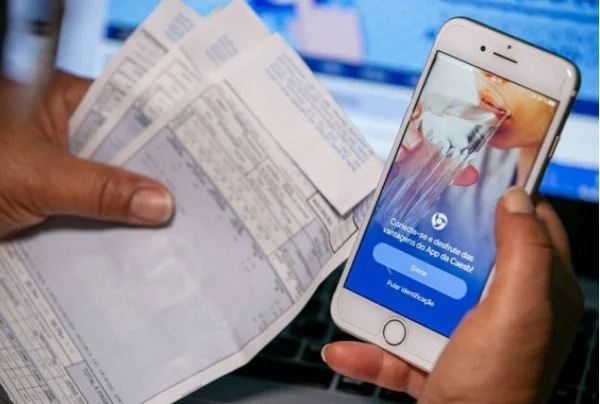 Pessoa segurando conta de água e celular - Metrópoles