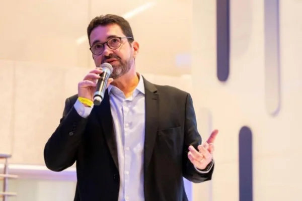 Imagens coloridas mostram homem branco, de óculos e barba, cabelos curtos, com camisa clara e paletó escuro, discursando durante evento