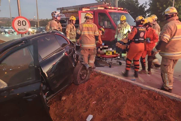 Foto colorida de bombeiros prestando socorro à acidente envolvendo um carro preto, que ficou gravemente destruído