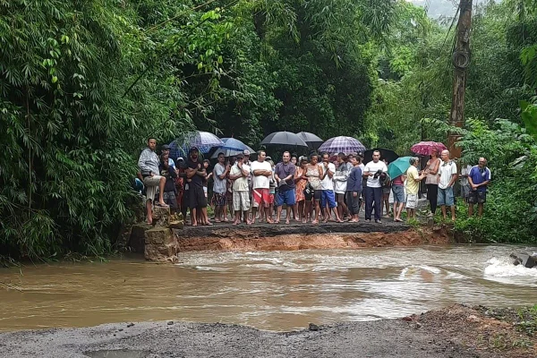 Grupo de pessoas paradas com guarda chuva em frente área alagada