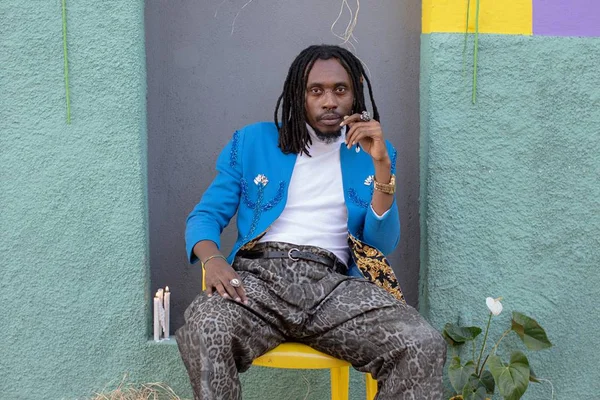 imagem colorida mostra rapper rincon sapiência. ele é negro, usa dreads e veste um casaco azul em cima de uma blusa branca. a calça tem estampa de onça. - metrópoles