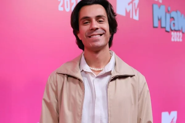 Pe Lu, vocalista do Restart, posa durante evento em uma parede com fundo rosa - Metrópoles