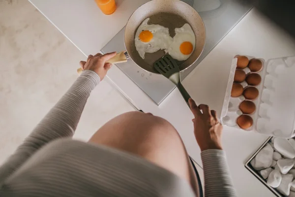 Mulher branca grávida fritando dois ovos frigideira