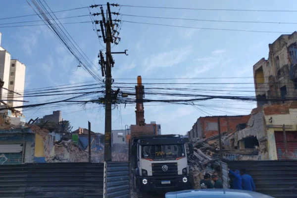 imagem colorida mostra caminhão e trator trabalhando em demolição de imóveis. é possível ver entulhos e uma separaçãodo terreno