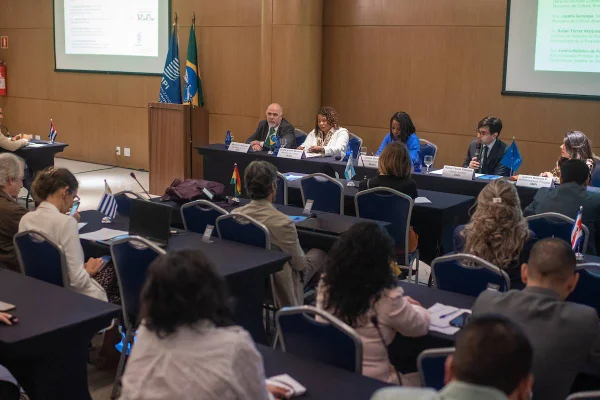 Fotografia colorida mostrando quatro pessoas em mesa na frente de várias pessoas durante seminário-Metrópoles