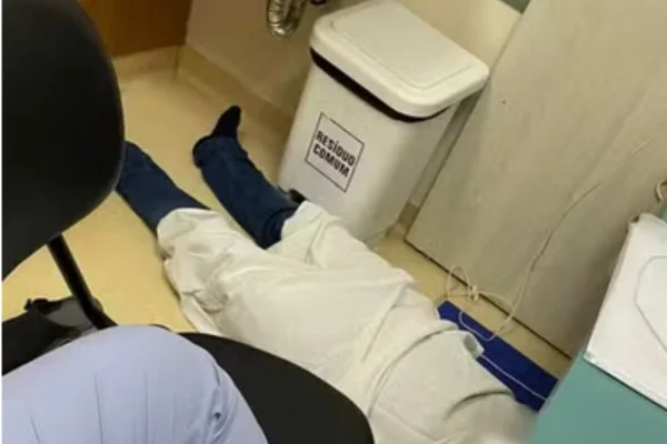 Jovem com jaleco branco deitado em chão d ehospital - Metrópoles