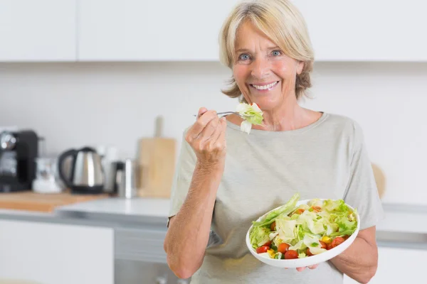 Foto colorida de mulher em cozinha comendo salada - Metrópoles