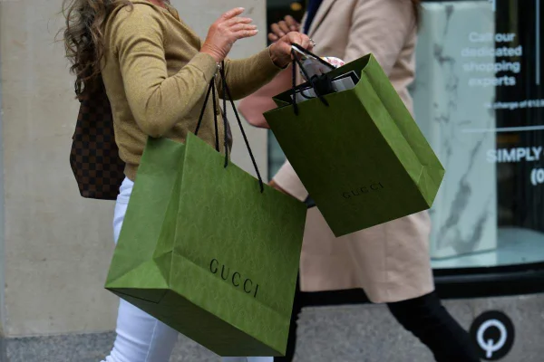 A imagem mostra uma mão feminina carregando duas sacola verdes da Gucci