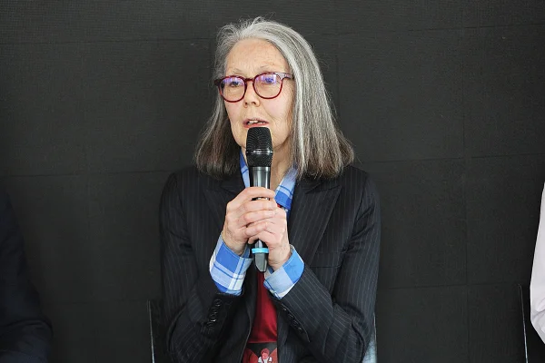 Imagem colorida da autora Anne Carson com microfone na mão - Metrópoles