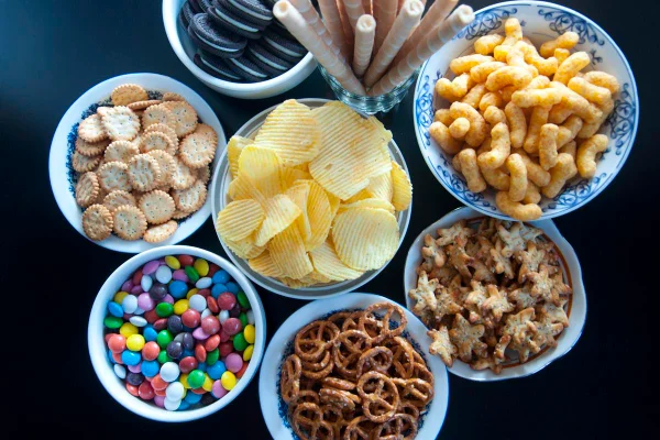 Foto colorida de várias tigelas com balinhas, biscoitos, doces e salgadinhos - Alimentos ultraprocessados, perda de peso