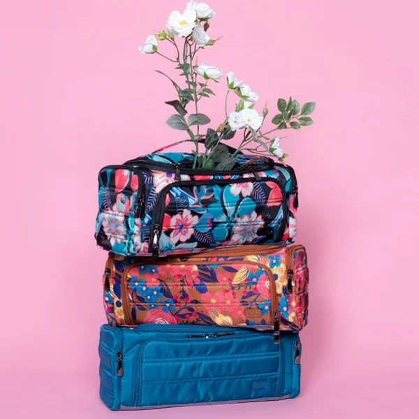 Três bolsas necessaires, estampadas, uma em cima da outra. O fundo da foto é rosa.