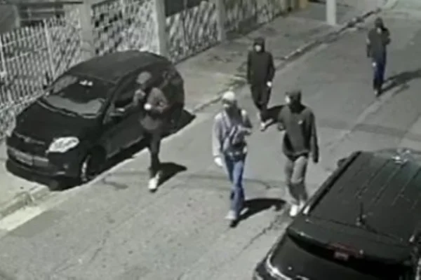 Imagem em preto e branco de cinco homens encapuzados andando em rua; eles são suspeitos pela morte de um idoso - Metrópoles