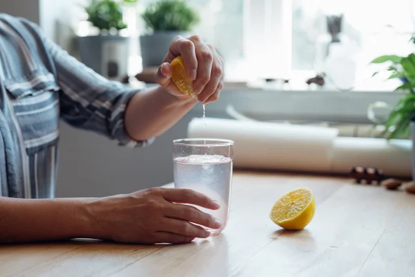 Uma mão masculina espreme um limão num copo com água - Metrópoles
