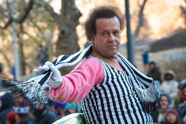 foto colorida de homem vestindo roupa listrada e segurando lenço na mesma estampa; ele é Richard Simmons - metrópoles