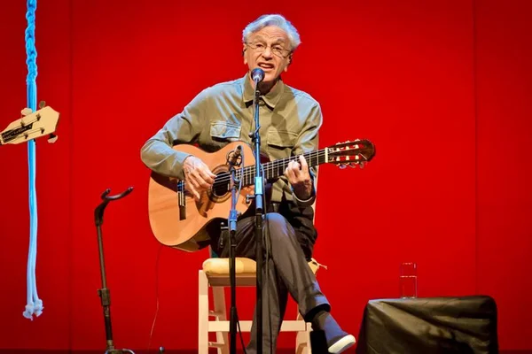 Foto colorida de Caetano Veloso sentado segurando violão - Metrópoles