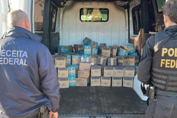 Dois agentes da Polícia Federal (PF) em pé em cima de uma van cheia de caixas de vinho