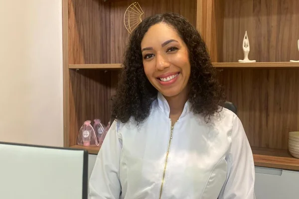 Foto colorida de de mulher usando roupa branca, sentada, sorrindo para foto - Metrópoles.