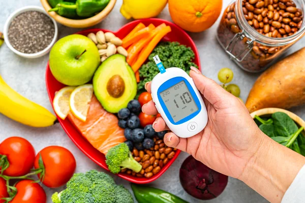 Foto colorida de alimentos sobre uma mesa, enquanto uma mãe feminina segura um medidor de glicose. - Metrópoles