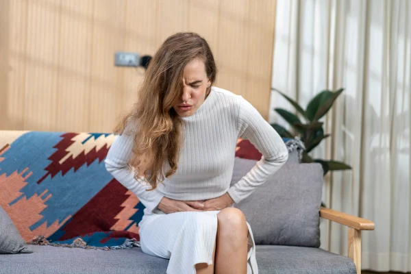 Foto colorida de mulher sentada em sofá com dores abdominais - Metrópoles