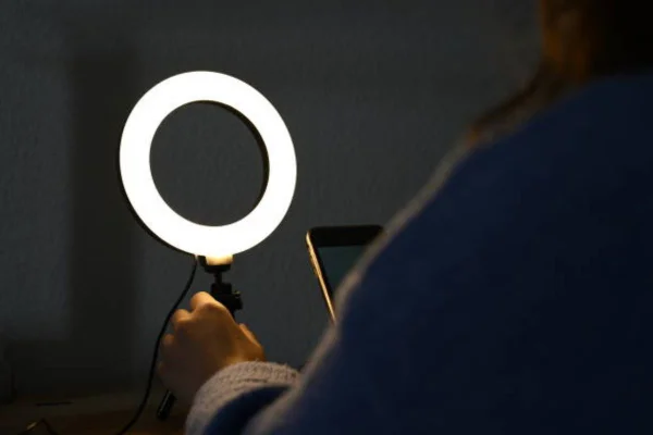 imagem colorida de uma ring light e uma mulher de costas mexendo no celular