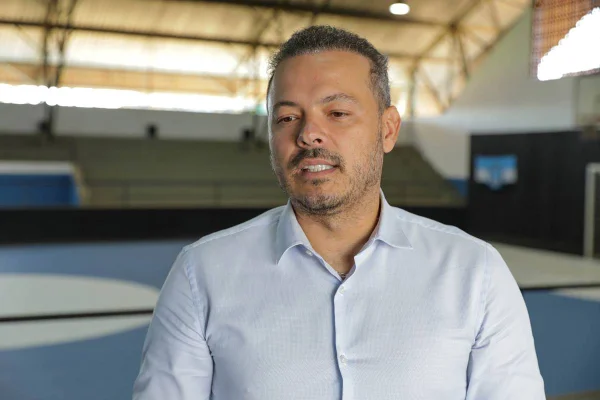 Fotografia de homem em ginásio de esportes. Ele está vestido com camisa azul