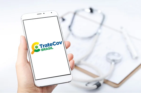 Imagem de divulgação do aplicativo TrateCov, idealizado pelo governo Bolsonaro. No detalhe, uma pessoa segura um celular com o software aberto com um estetoscópio desfocado ao fundo - Metrópoles