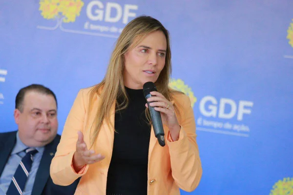 Mulher loira de roupas sociais falando com microfone em evento do GDF