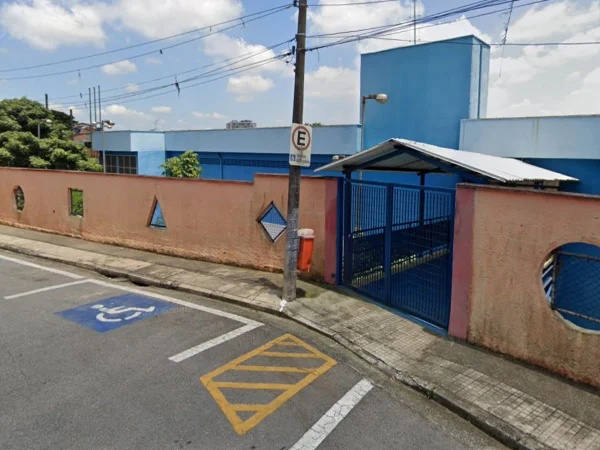Foto colorida mostra fachada de escola com muro vermelho e portão azul.