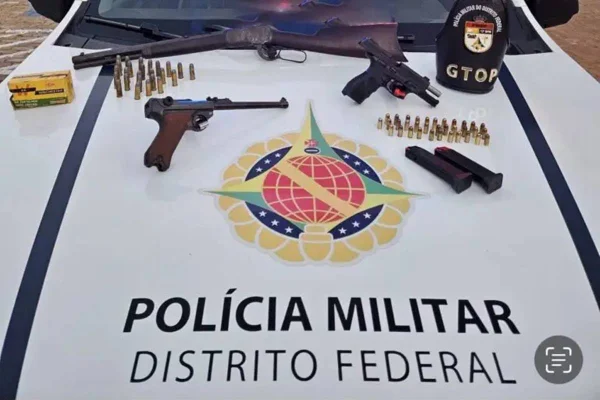 Foto colorida de armas de fogo em cima de capo de carro da PMDF