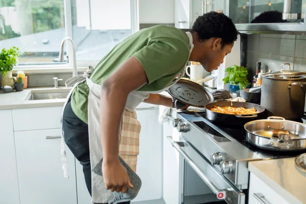 Homem fazendo o jantar, levantando a tampa da panela, cheirando o prato de macarrão, alimentação saudável, estilo de vida saudável, cozinhando comida. Metrópoles