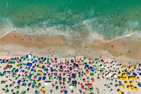 Foto colorida tirada de cima, onde a paisagem é uma praia lorada de gente