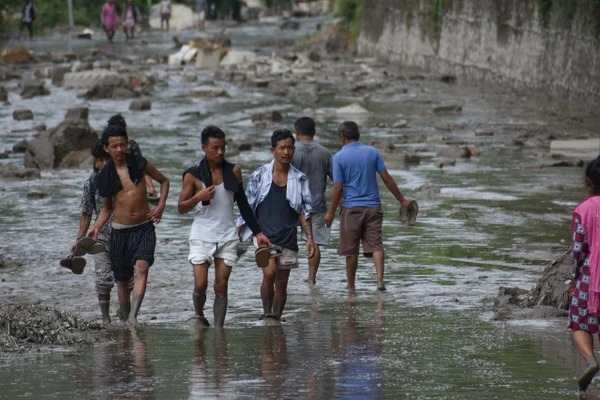 Pessoas caminham por uma estrada coberta pelas águas de uma enchente em Nuwakot, Nepal