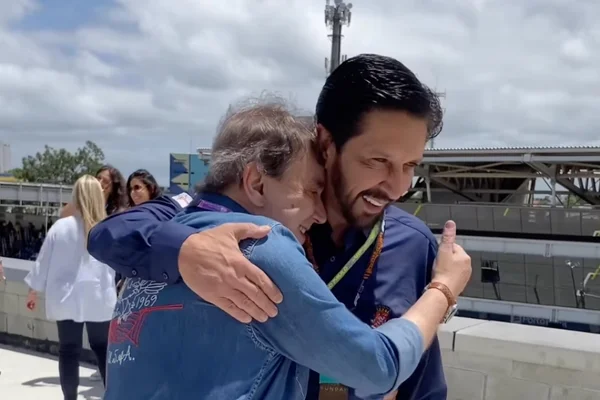 Imagem colorida mostra Ricardo Nunes, homem branco, de cabelo e barba pretos, vestindo camisa azul, abraçando um homem branco, grisalho, de camisa jeans. Eles estão na pista do Autódromo de Interlagos - Metrópoles