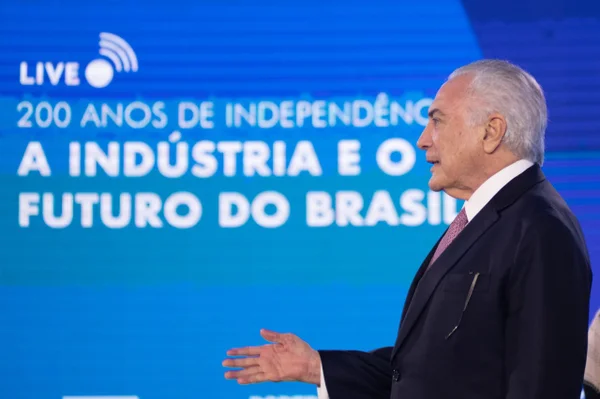 Ex-presidente da República, Michel Temer fala durante evento da CNI. Ele usa terno e está diante de telão azul frente a pulpito com microfone - Metrópoles