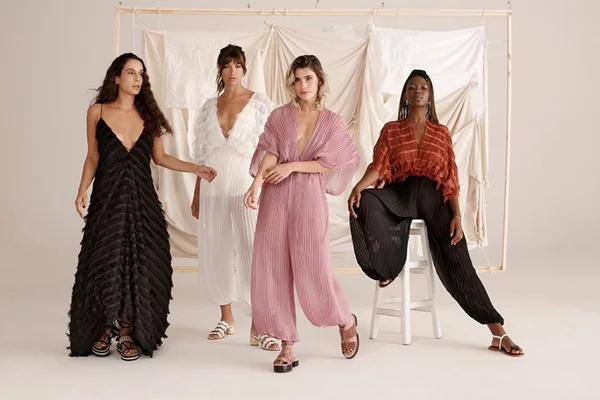 Modelos mulheres sentadas com roupas em tons de rosa, branco e marrom