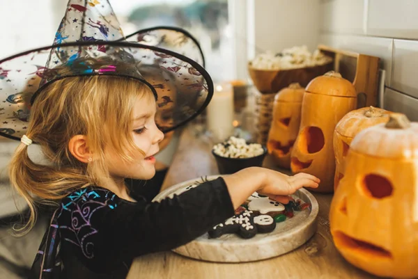 Foto colorida de menina fantasiada de bruxa pegando doces em festa de Halloween - Metrópoles