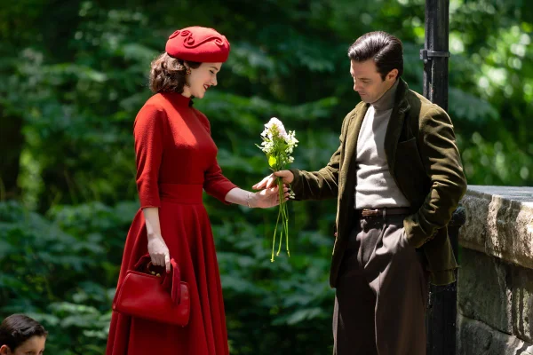 Cena de gravação da série Maravilhosa Sra Maisel, do Prime Video. Na foto é possível ver duas pessoas roupas usadas na década de 1960: uma mulher branca com cabelos curtos ondulados, de casaco, chápeu e bolsa, tudo vermelho; e um homem branco, jovem, de cabelo preto e com calça e blazer marrom