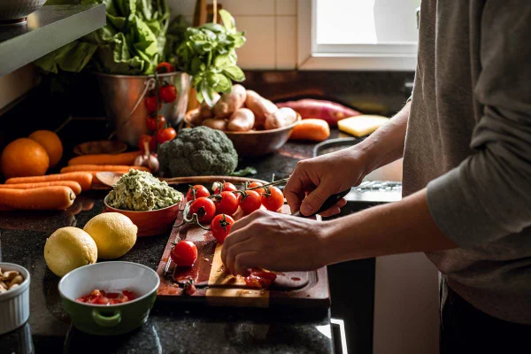 Moça cortando tomate com diversos alimentos na bancada