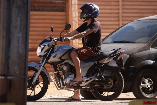 Imagem colorida de um homem em uma moto, usando capacete com a viseira levantada